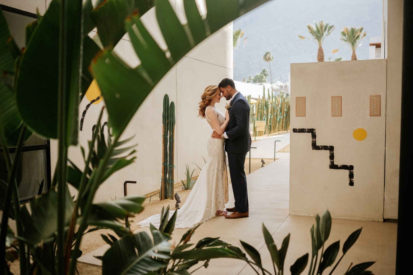 Romantic couple sharing a quiet moment in a modern desert courtyard surrounded by tropical plants and cacti, with mountain views in the background