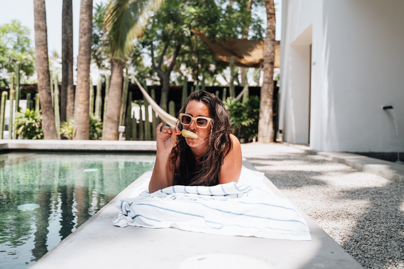 Woman relaxing poolside at a boutique hotel, eating a popsicle on a striped towel