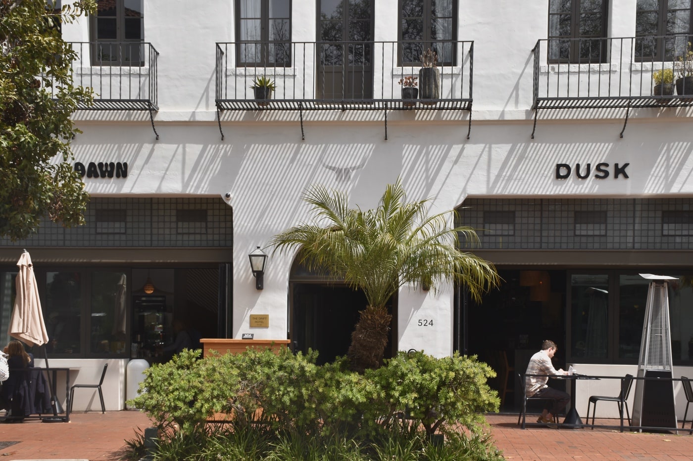 White stucco boutique hotel facade with ‘Dawn’ and ‘Dusk’ entrances and patio seating