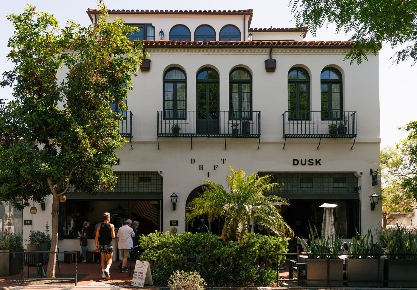 Spanish Colonial Revival building with "DRIFT" and "DUSK" signage, featuring arched windows, balconies, and palm trees.