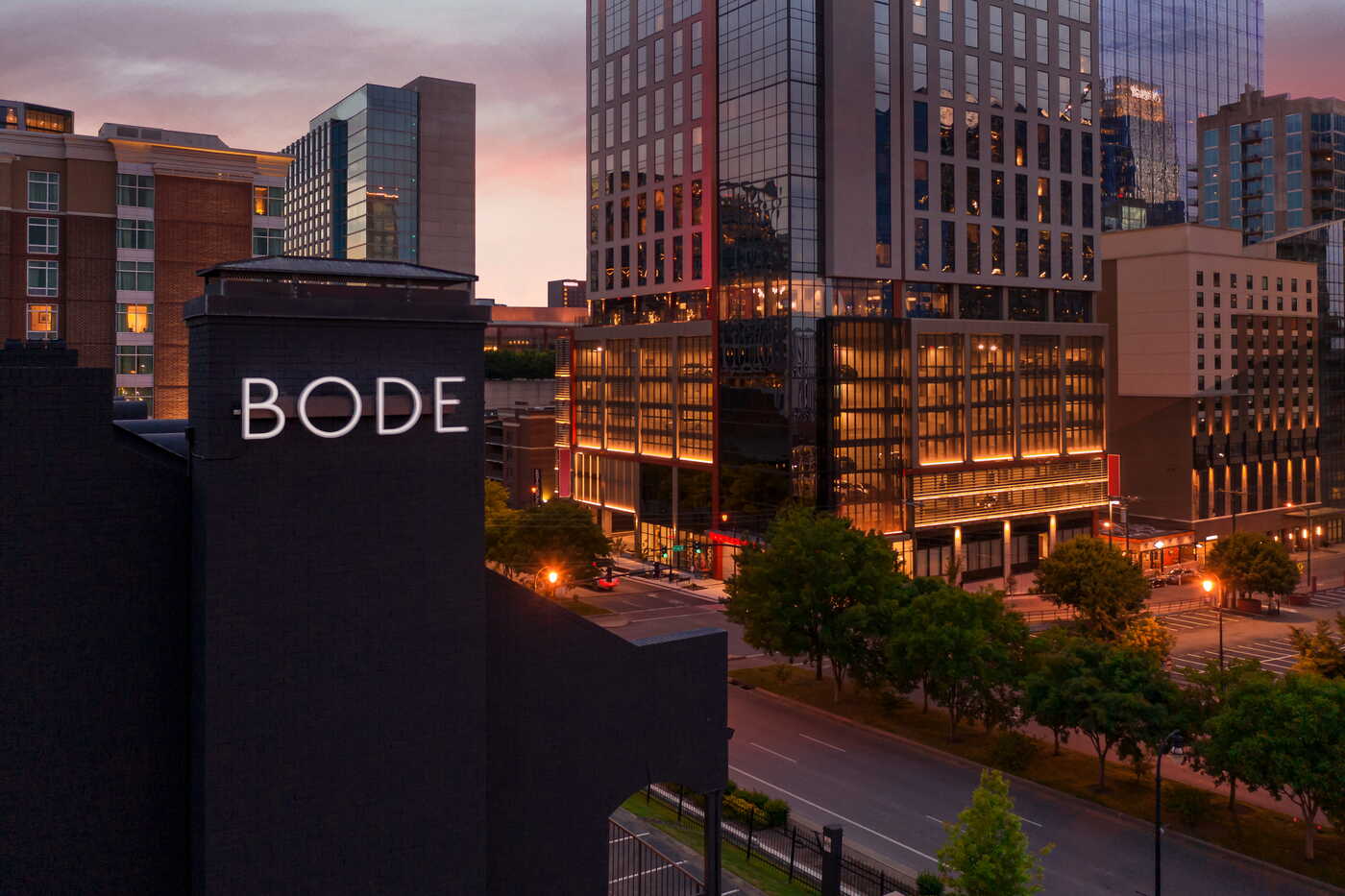 Illuminated Bode hotel sign on a dark brick building overlooking the Nashville downtown skyline at dusk
