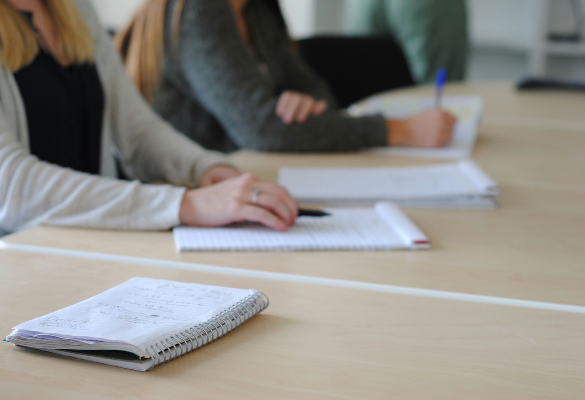 Two women sitting at a conference table, their arms resting on papers with notes, their faces are cropped out.