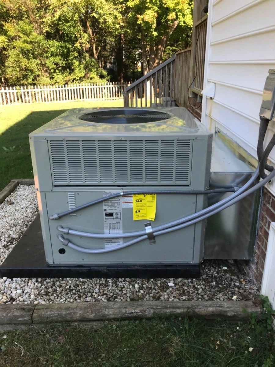 Large outdoor air conditioning unit beside a house, surrounded by pebbles. 