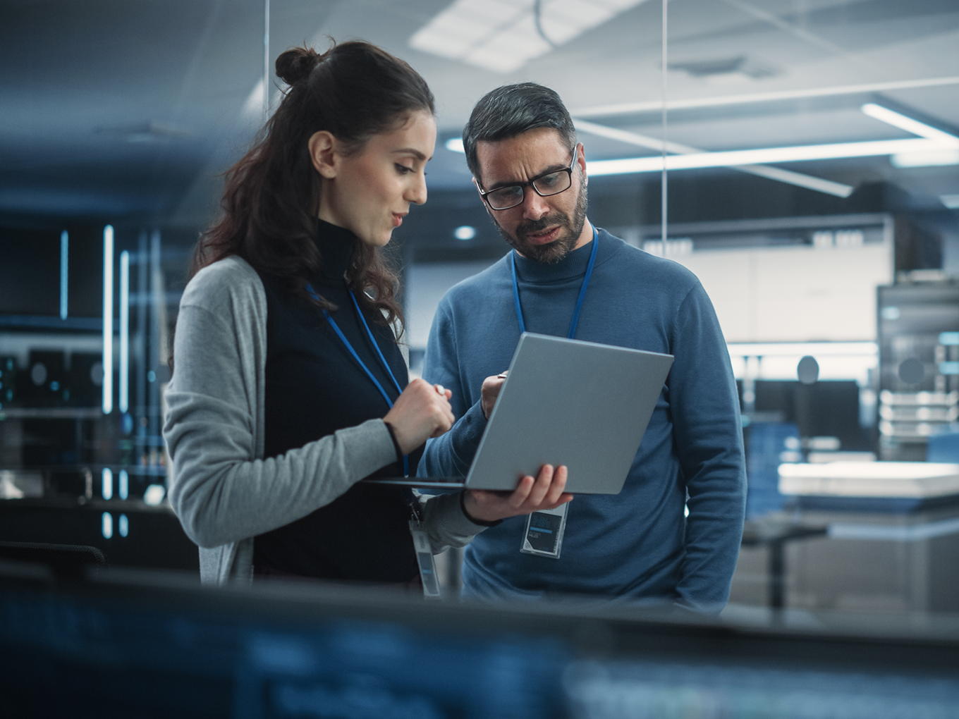 Two colleagues in an office looking at a laptop screen together, discussing work.