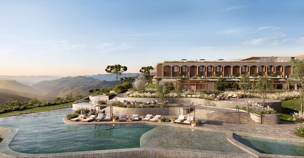 Piscina em resort de luxo com espreguiçadeiras e área verde, cercada por montanhas ao fundo ao pôr do sol.