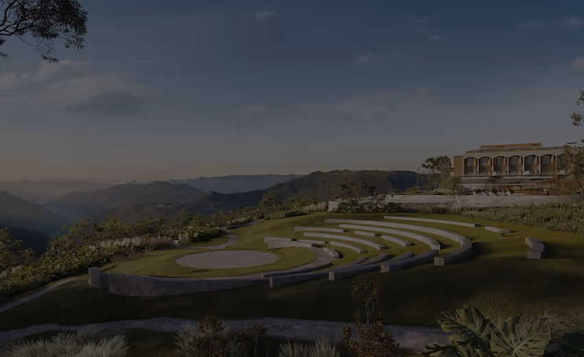 Anfiteatro ao ar livre com bancos em meia-lua e um palco circular, situado em uma área verde com vista para montanhas ao entardecer.