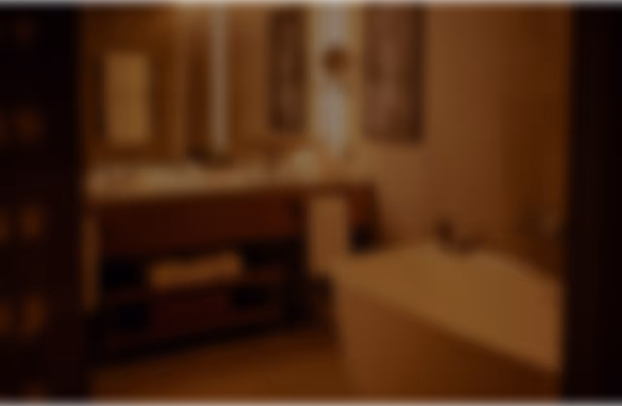 Banheiro com bancada de pia, espelho e banheira, em tons de marrom e iluminação suave.