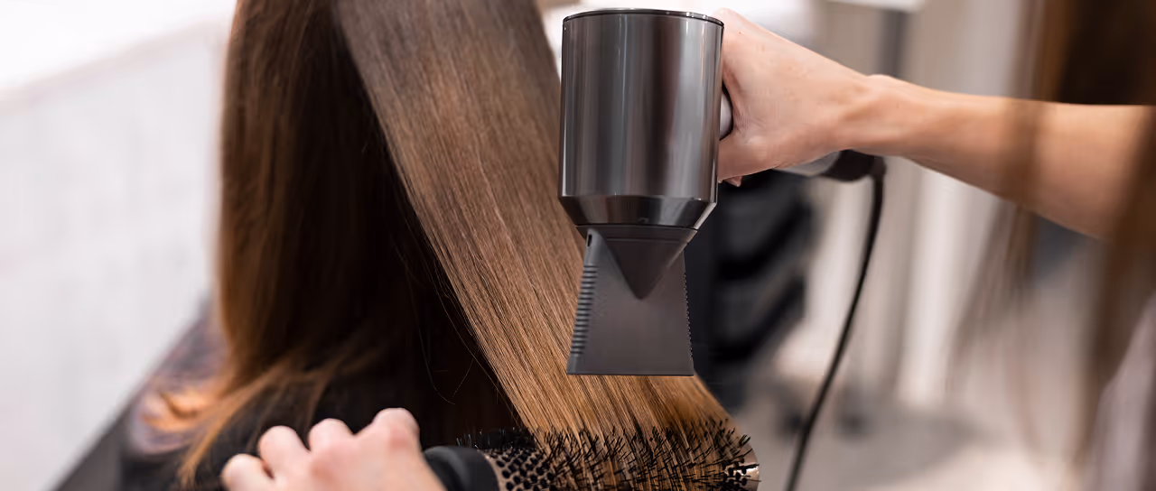 Pessoa secando o cabelo liso e castanho com secador e escova redonda preta.