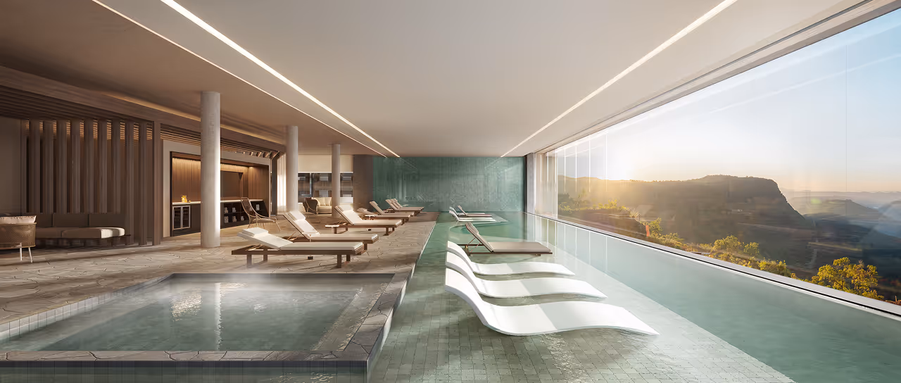 Piscina interna com espreguiçadeiras submersas e área de relaxamento com vista panorâmica para montanhas ao nascer do sol.