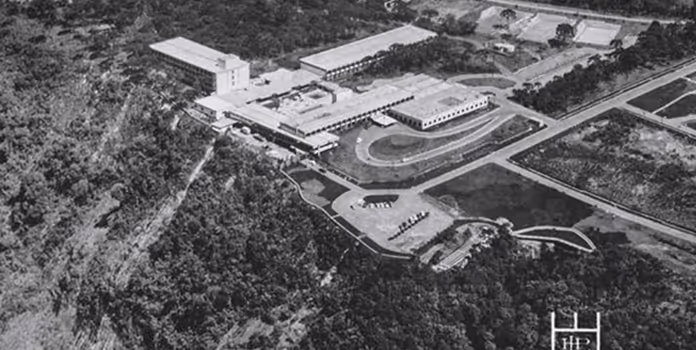 Imagem aérea em preto e branco de um complexo industrial ou universitário cercado por áreas arborizadas.