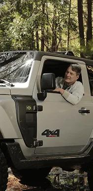 Homem sorridente dirigindo um veículo 4x4 diesel em área florestal.