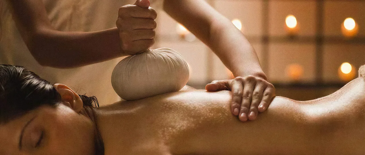 Pessoa recebendo massagem nas costas com bolsa térmica em ambiente de spa iluminado por velas.