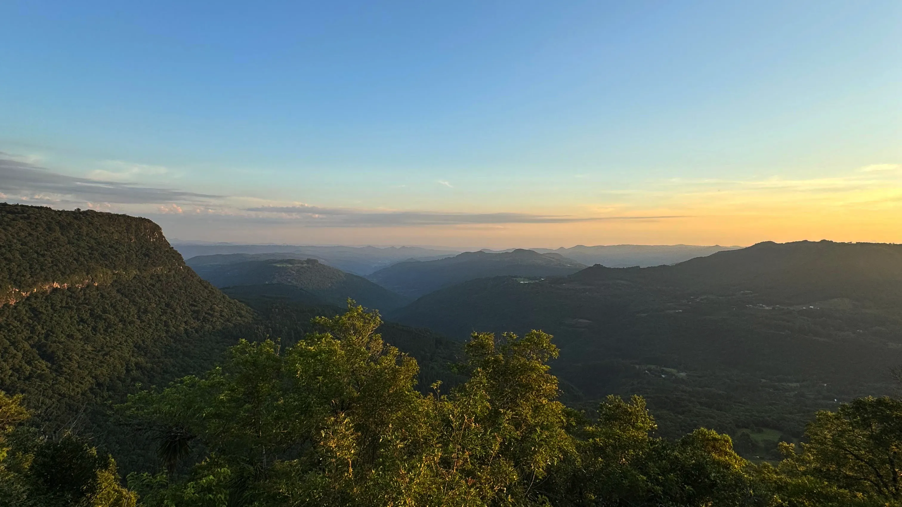 Vista panorâmica de montanhas cobertas por vegetação sob céu limpo ao pôr do sol.