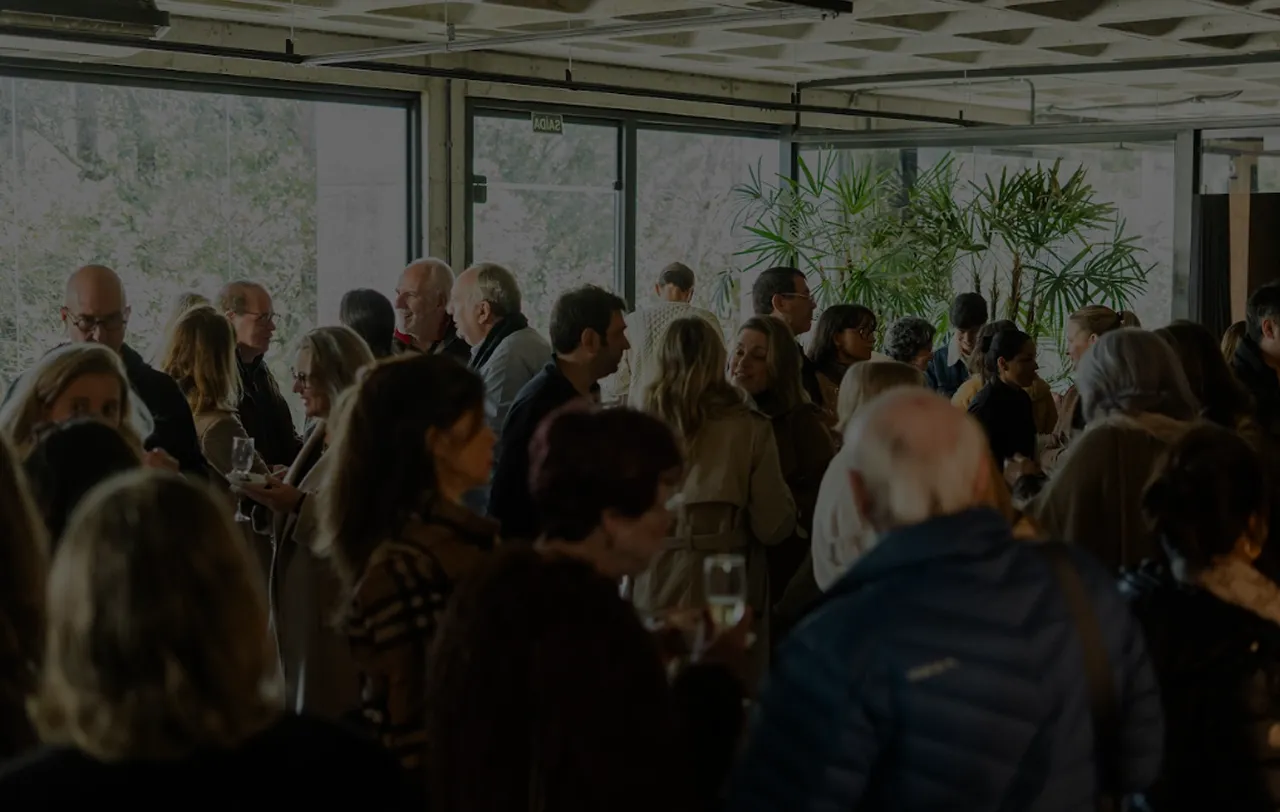 Grupo de pessoas conversando em um ambiente interno iluminado por luz natural de grandes janelas.