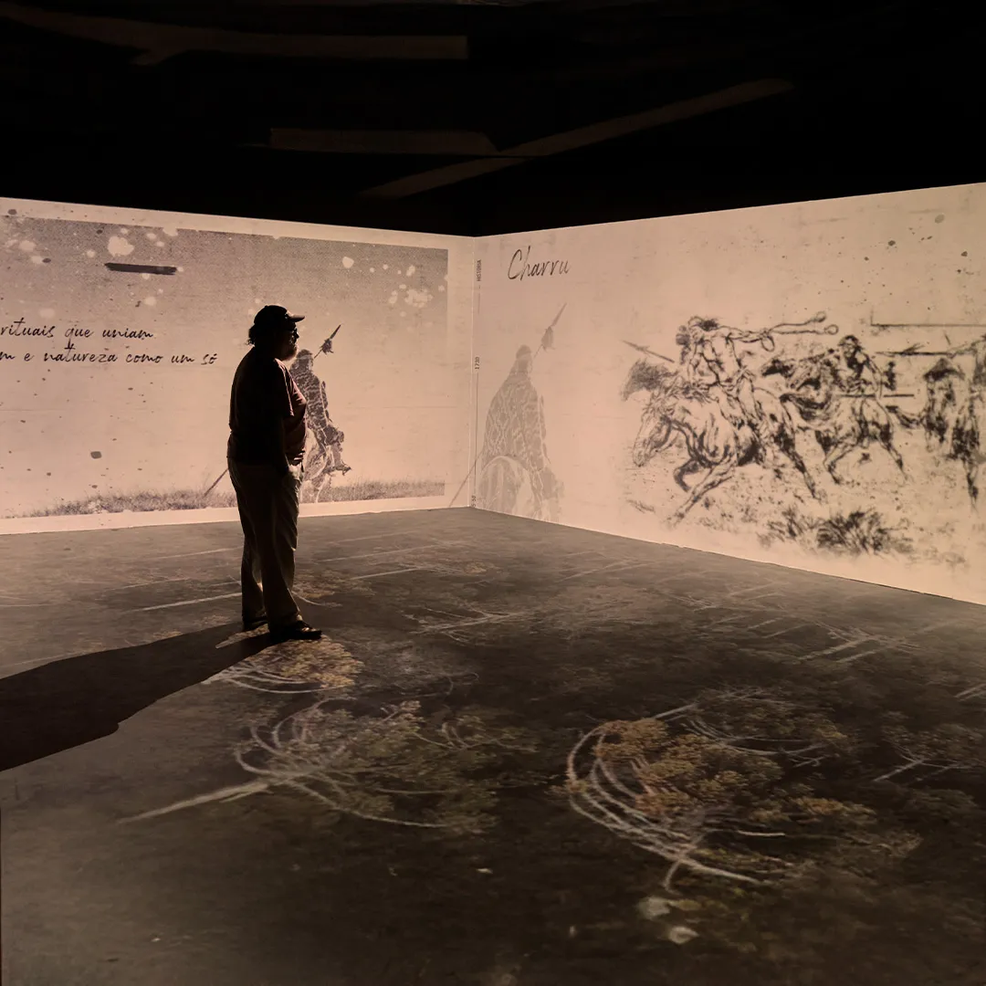 Homem observando projeção de desenhos em estilo antigo de cavaleiros com lanças em uma sala escura.