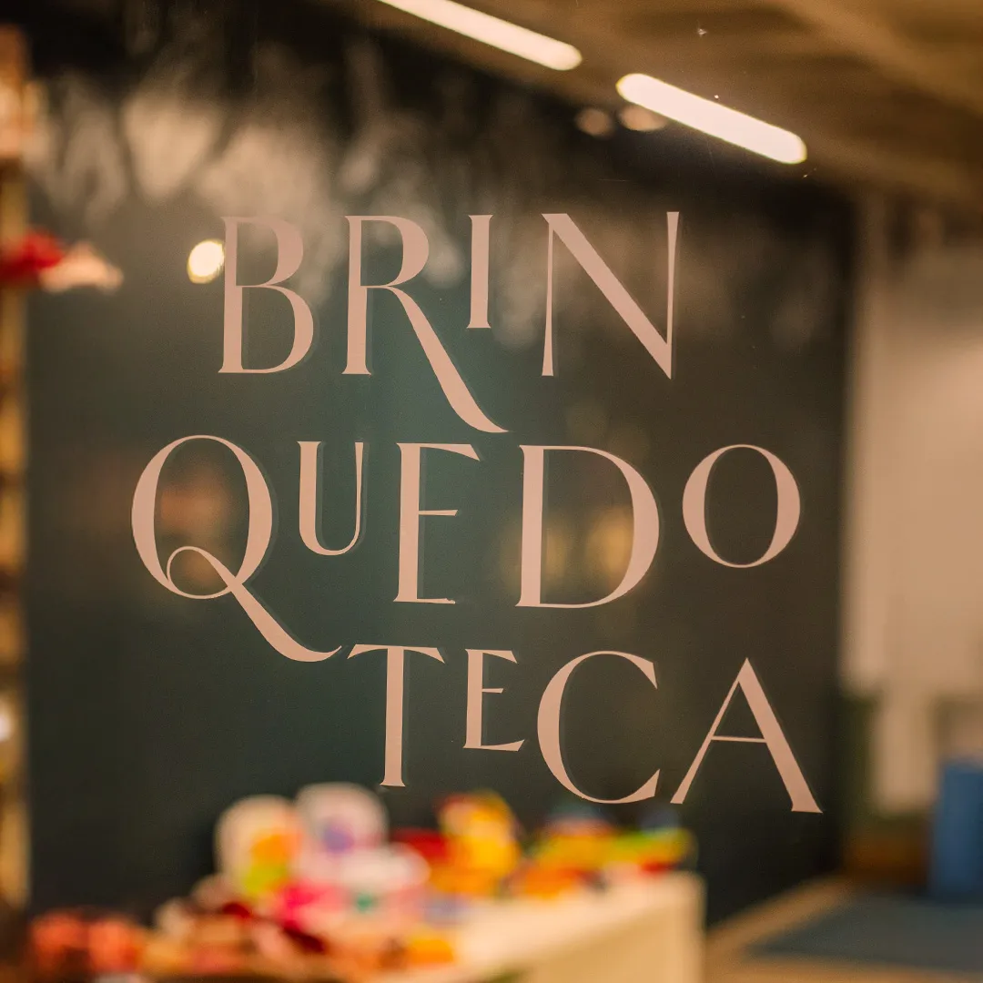 Letreiro com a palavra Brinquedoteca em letras grandes, com brinquedos coloridos desfocados ao fundo.