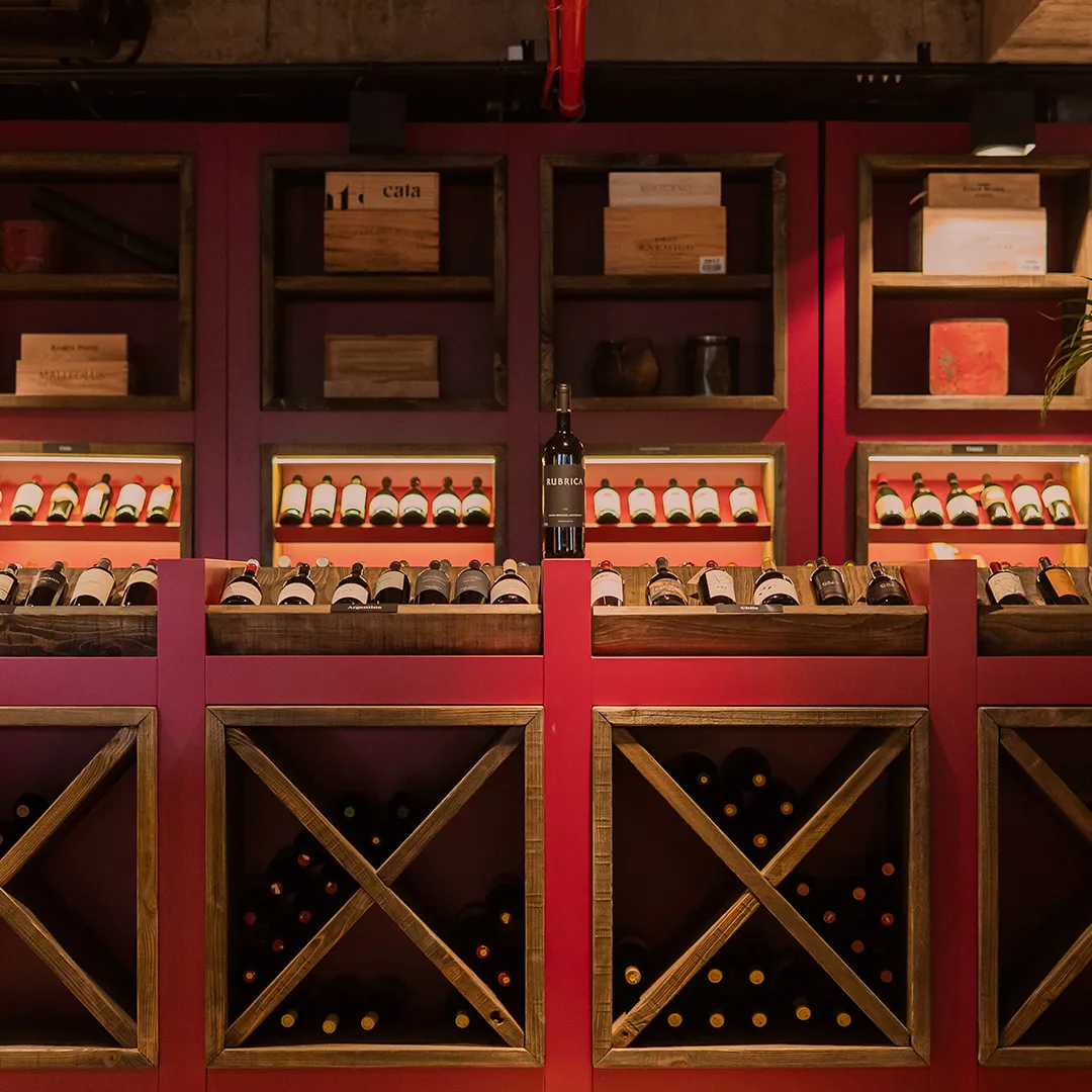 Adega com várias garrafas de vinho organizadas em prateleiras e compartimentos de madeira vermelha.