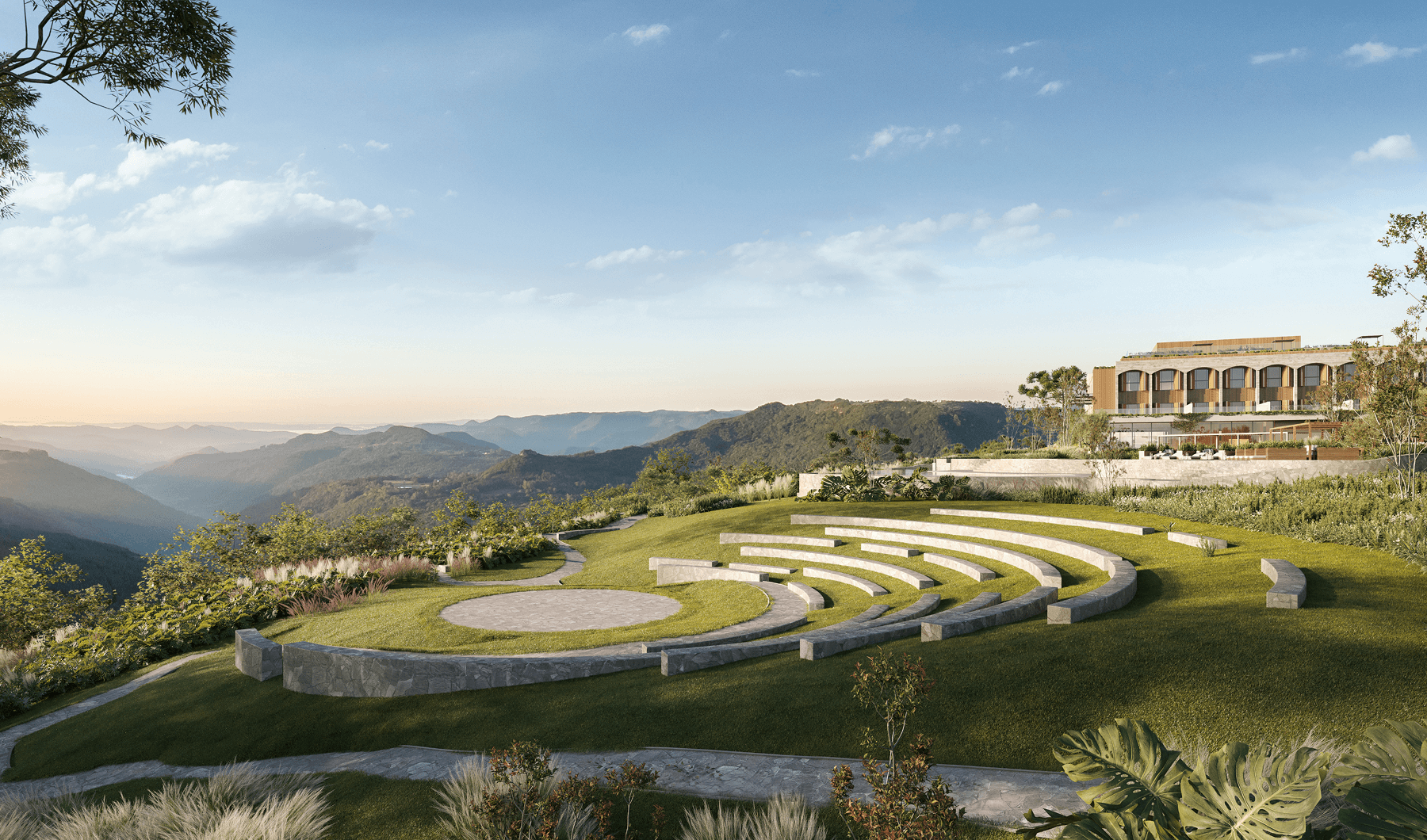 Anfiteatro ao ar livre em gramado com assentos de pedra e vista para montanhas sob céu azul com nuvens.