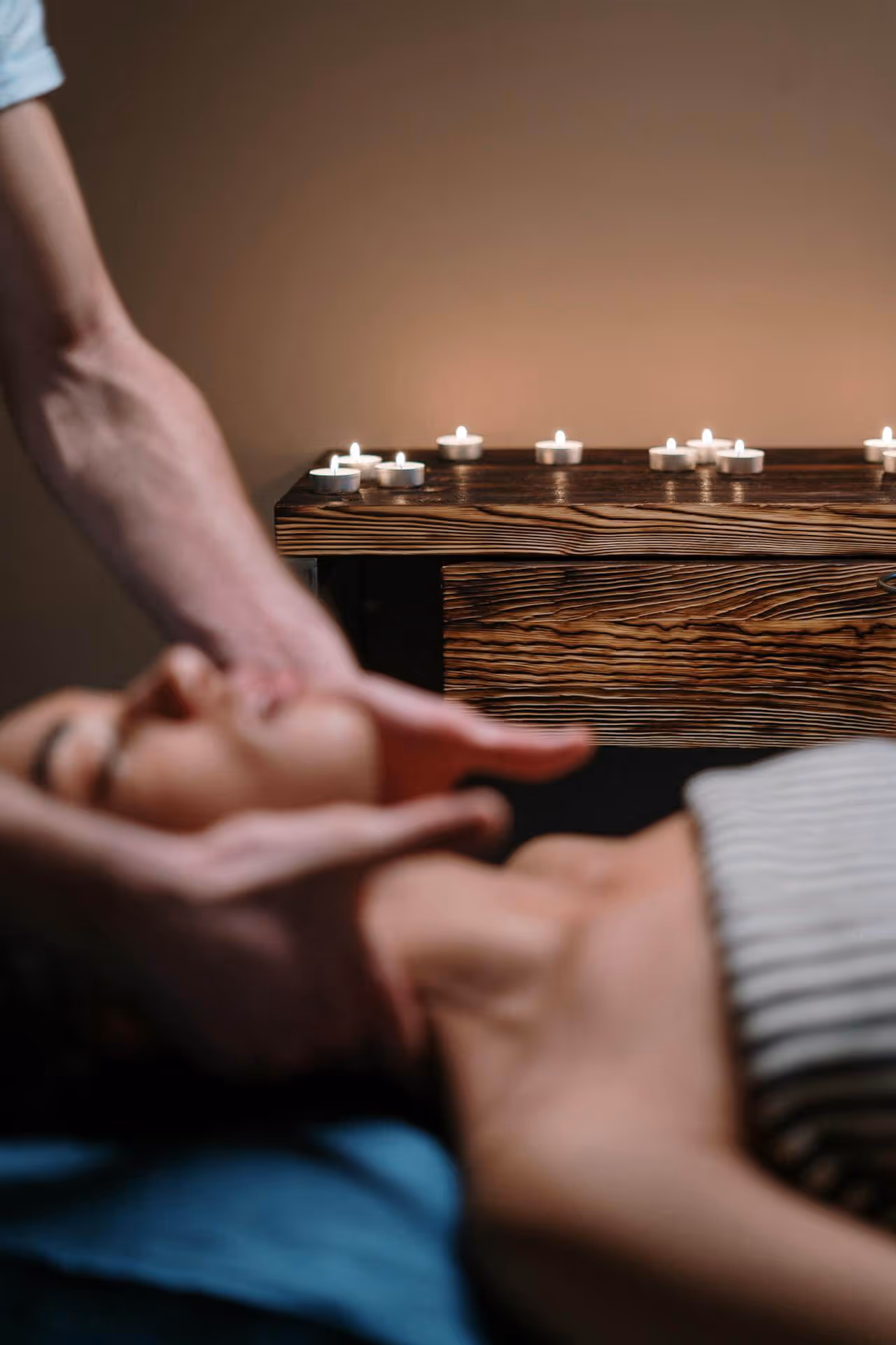 Person receiving a gentle facial massage with lit tea candles on a wooden surface in the background.
