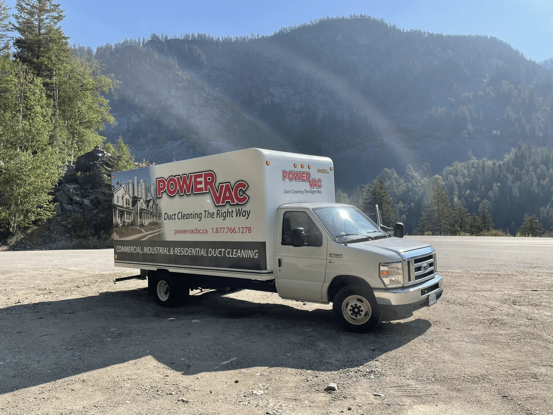 White PowerVac duct cleaning truck parked on a gravel area with forested mountains in the background.