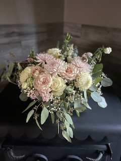 Bouquet of pastel-colored flowers including roses, chrysanthemums, and eucalyptus leaves on a dark surface.