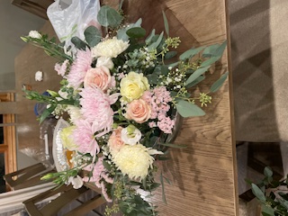 Bouquet of mixed flowers including pale pink roses, white carnations, and greenery on a wooden table.