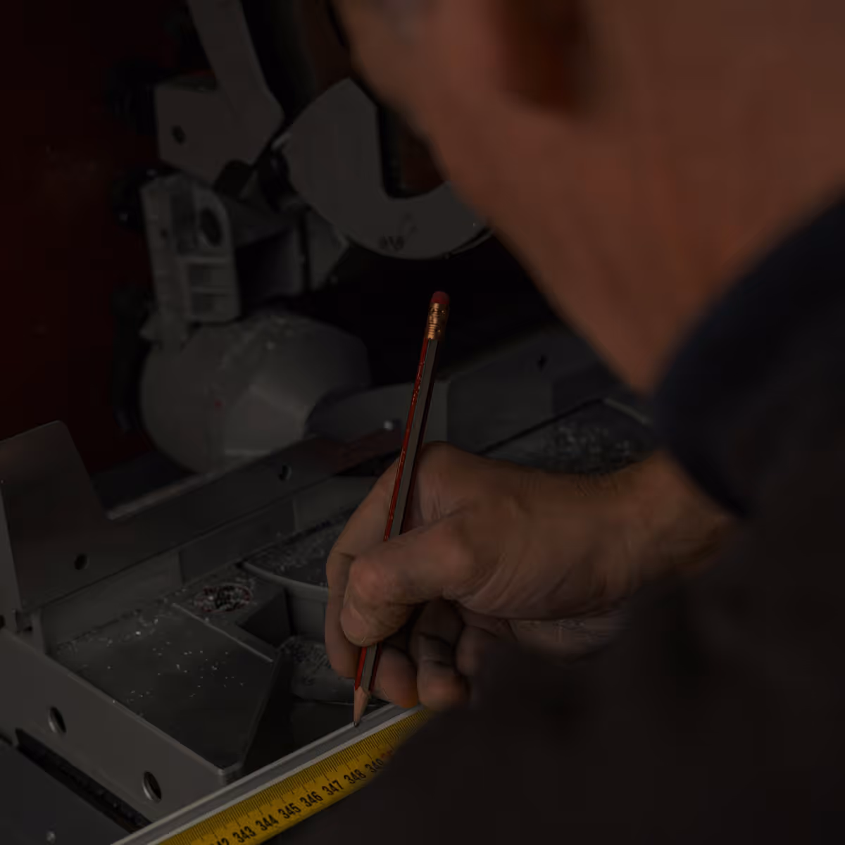 Person marking a measurement with a pencil on a surface next to a yellow measuring tape.
