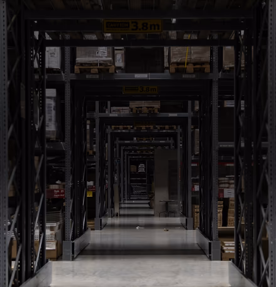 Long aisle in a warehouse with metal shelving units stacked with boxes and pallets.