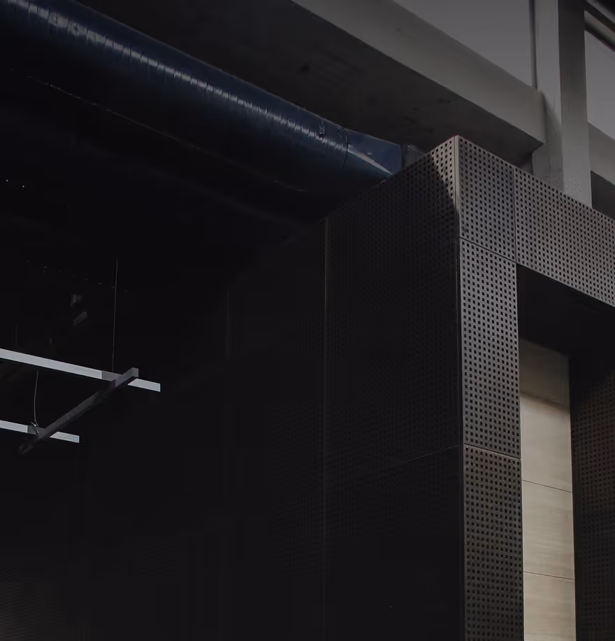 Dark interior view of a modern building corner with perforated metal panels and exposed ceiling ducts.