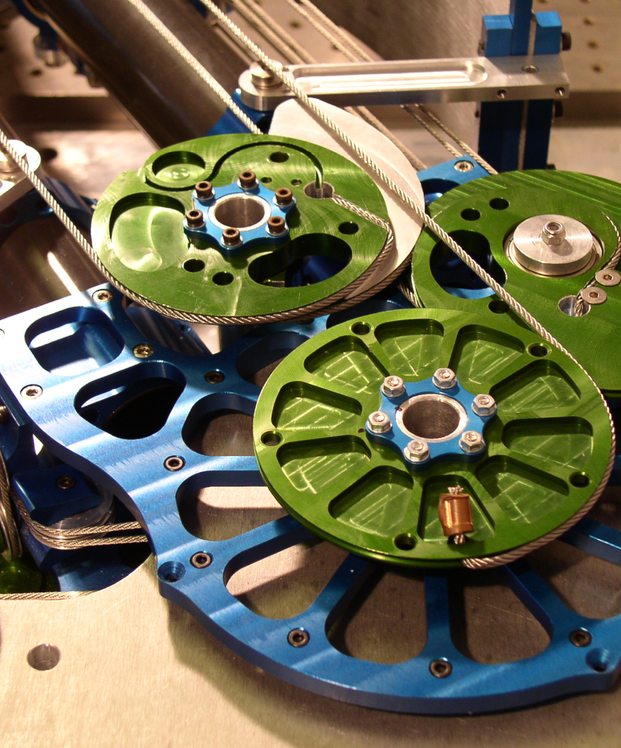 Close-up of a mechanical assembly featuring green and blue metal pulleys connected by steel cables.