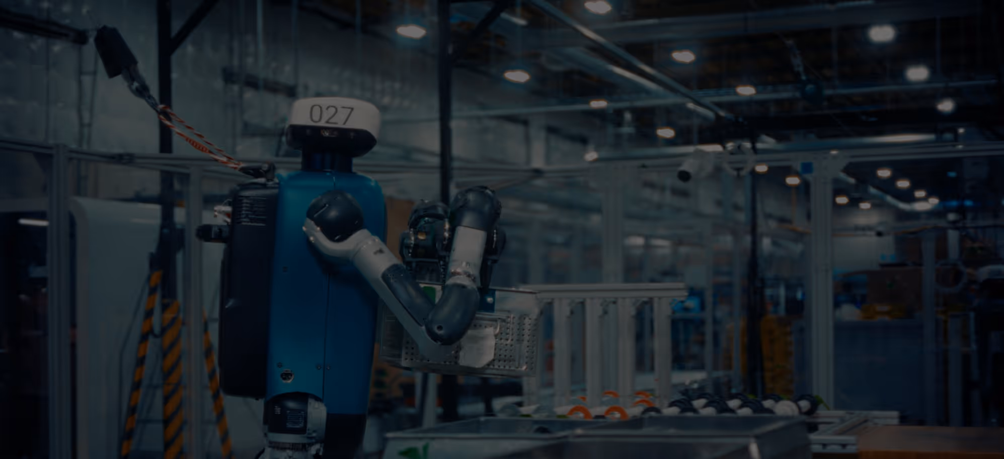 Blue robot with number 027 on its head holding a tray in an industrial factory setting.