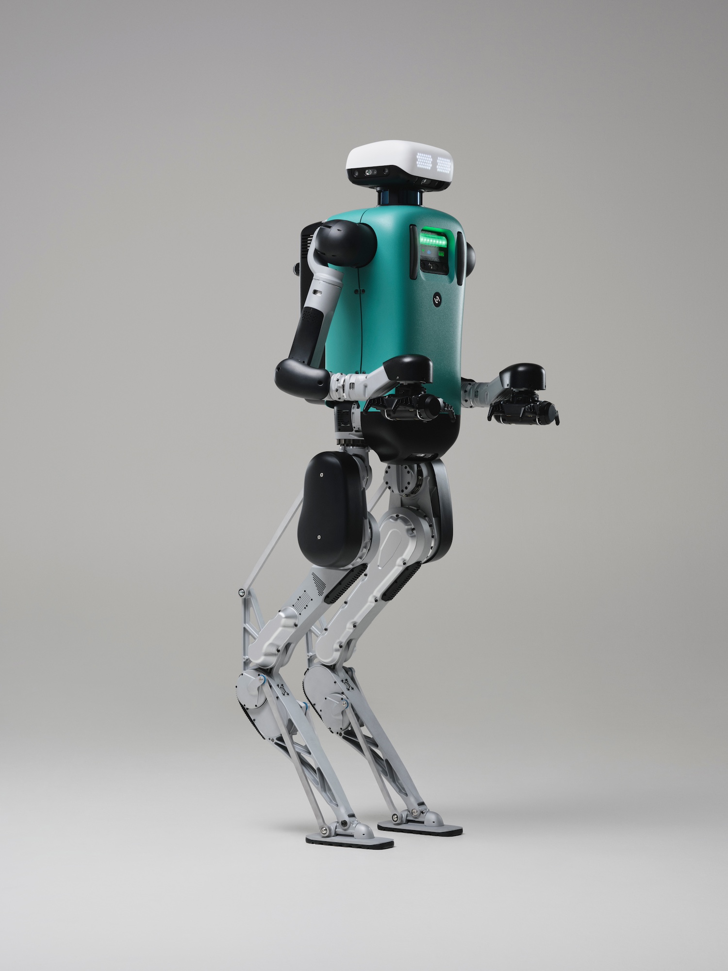 Bipedal robot with teal torso, white and black limbs, and digital face on a white background.