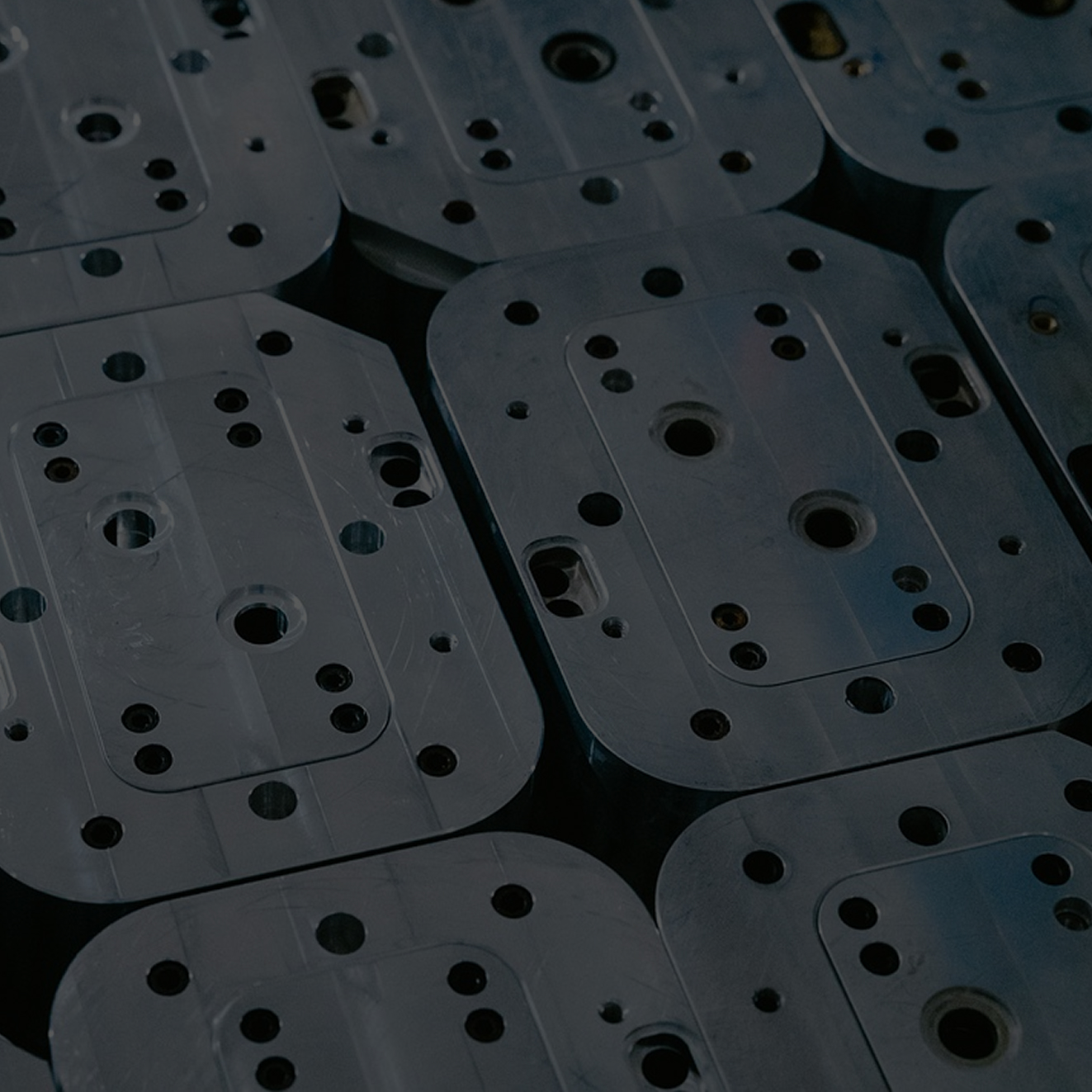 Close-up of stacked rectangular metal plates with various drilled holes.