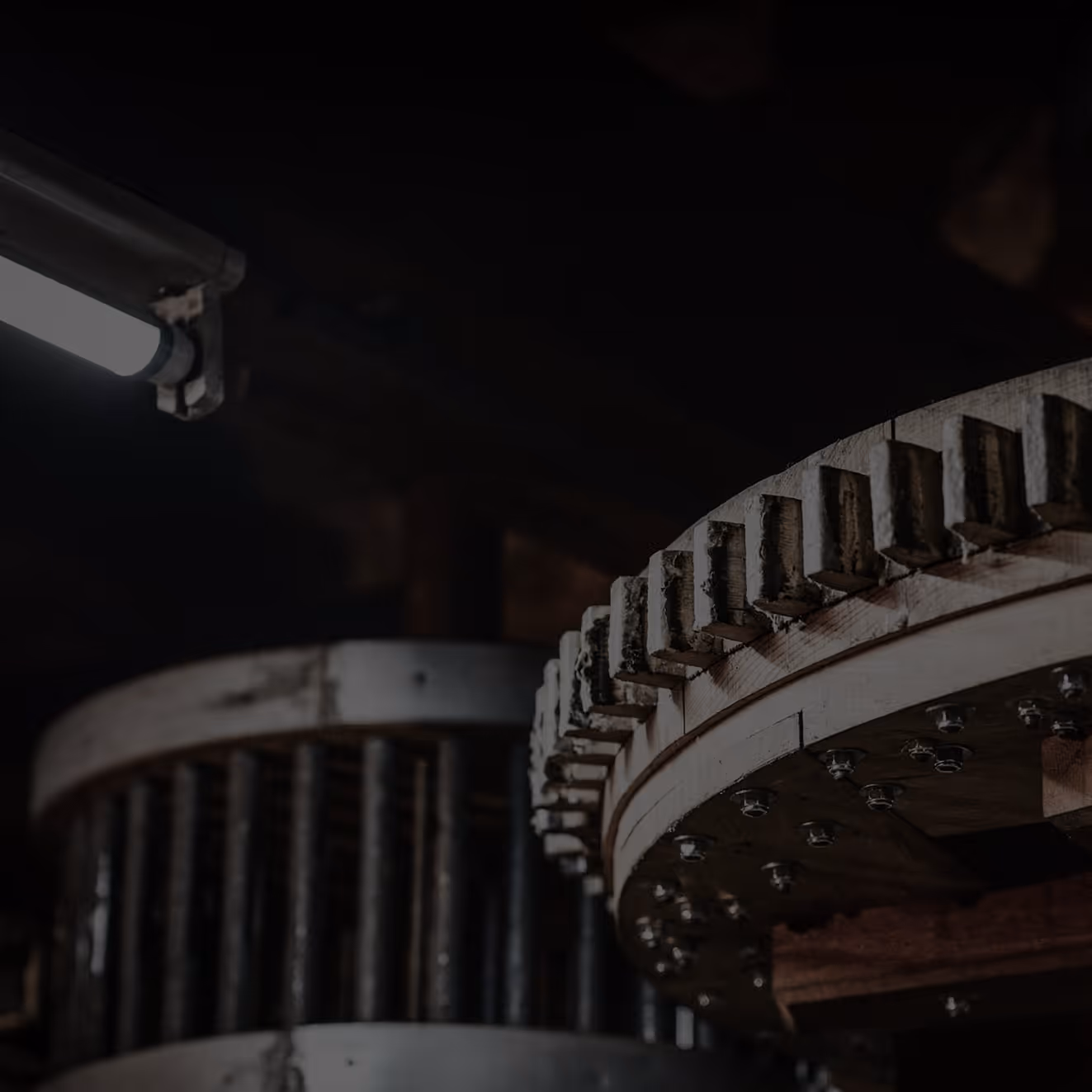 Close-up of large industrial wooden gears with metal bolts in a dimly lit environment.