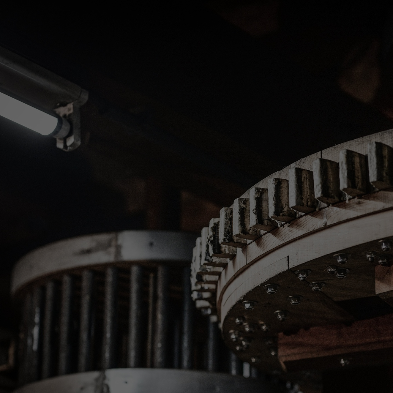 Close-up of large industrial wooden gears with metal bolts in a dimly lit environment.