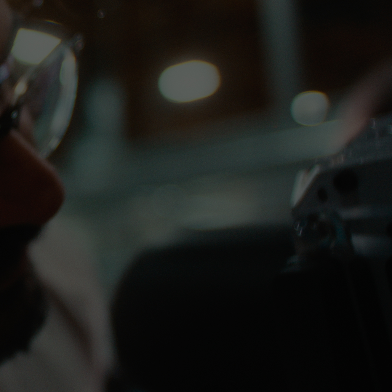 Close-up of a person wearing glasses focusing on operating a camera or similar device in a dimly lit environment.