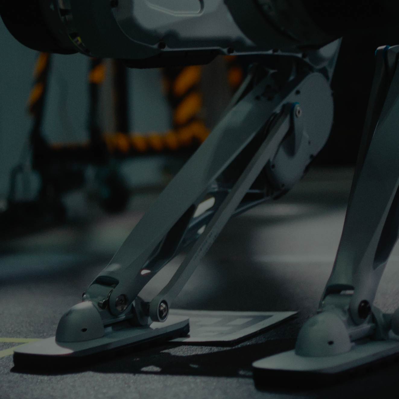 Close-up of robotic legs with mechanical joints standing on a dark surface.