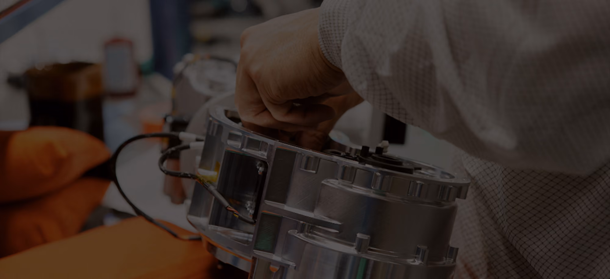 Person's hand working on a metallic mechanical component with wires in a technical workspace.