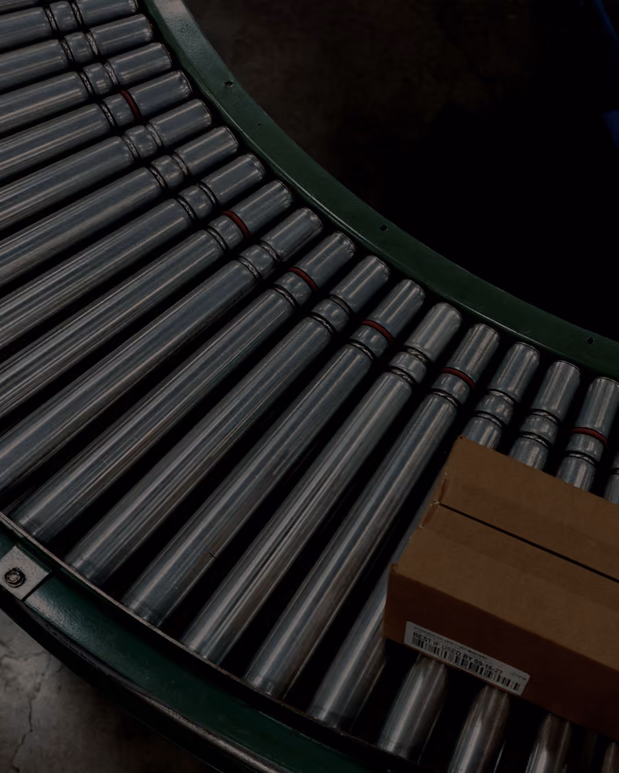 Close-up of a curved conveyor belt with metal rollers transporting a brown cardboard box.