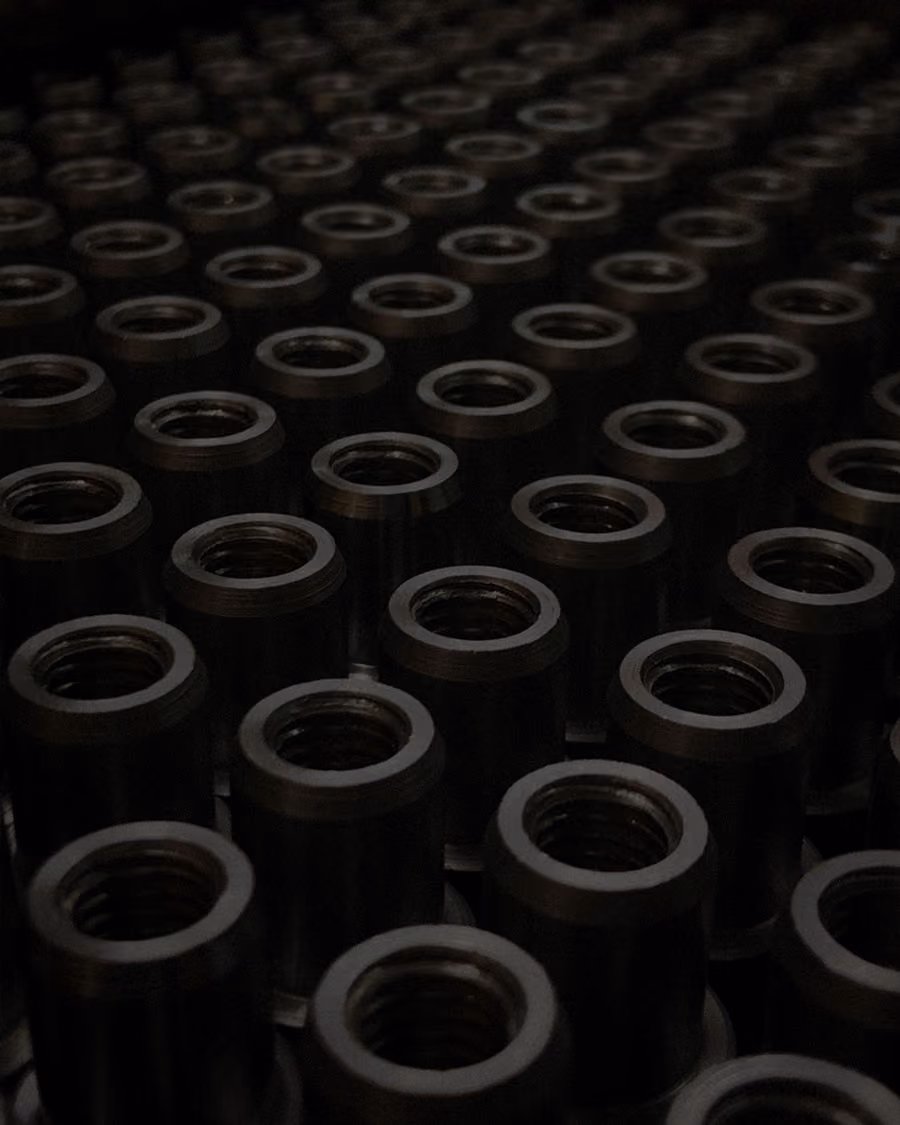 Close-up view of many identical dark cylindrical metal components with internal threading arranged in rows.