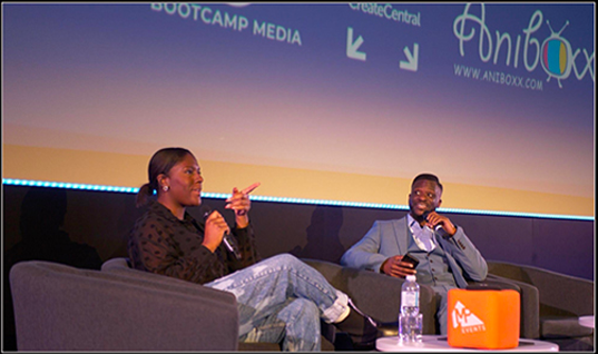 Two people seated on stage engaged in a panel discussion, each holding a microphone.