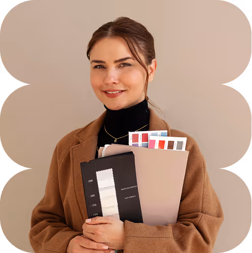 Smiling woman in brown coat holding fabric and color swatches in front of beige background.