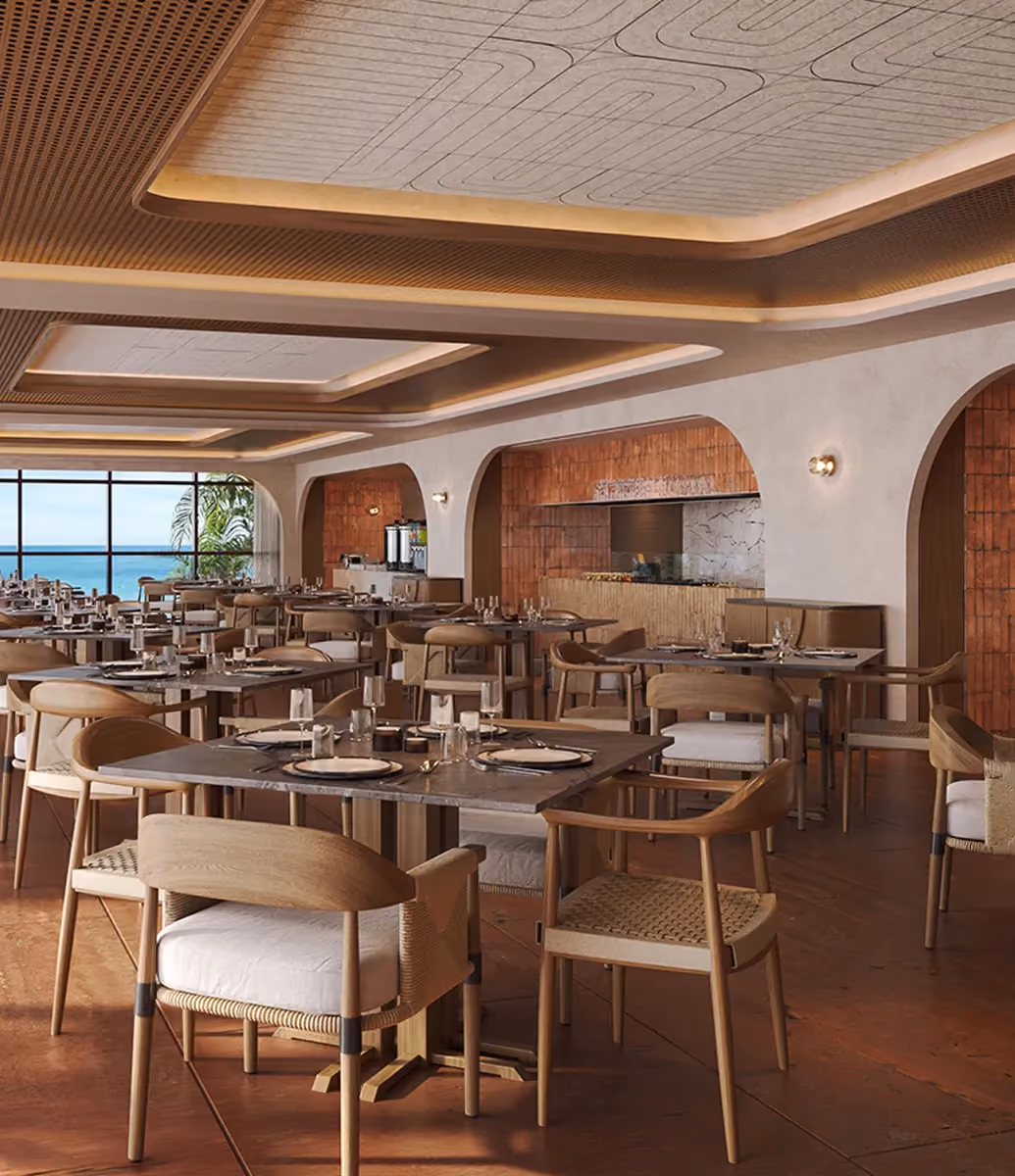 Spacious, modern restaurant interior with wooden chairs, square tables set with plates and glasses, warm lighting, terracotta floor, and large window showing a sea view.