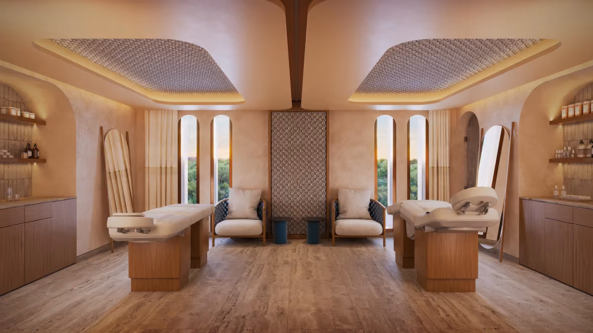 Symmetrical spa room with two massage tables, two cushioned armchairs, matching small tables, tall mirrors leaning against the walls, wooden cabinets with bottles and jars, and tall narrow windows showing greenery outside.
