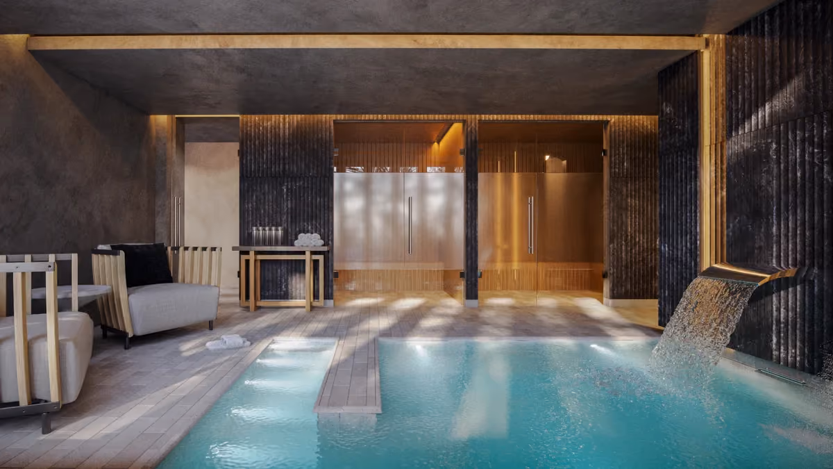 Indoor spa area with a modern rectangular pool featuring a water cascade on the right side, surrounded by light-colored tile flooring and dark textured walls, with two frosted glass doors and wooden seating with gray cushions on the left.