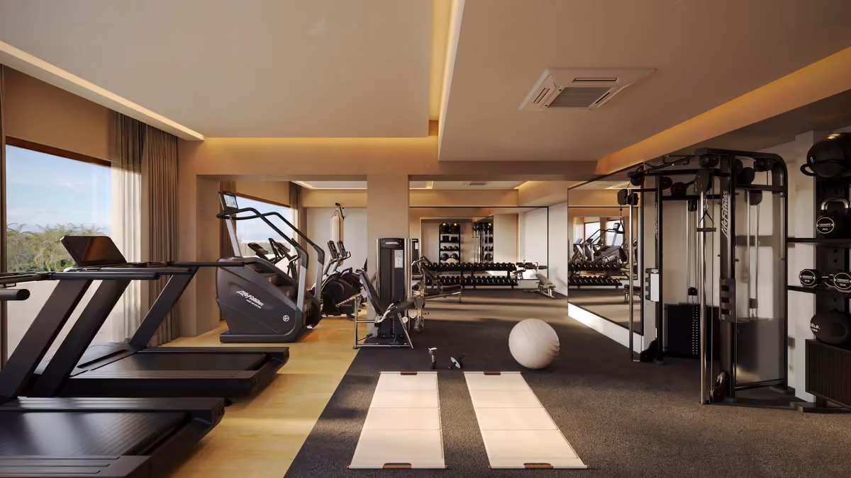 Bright, spacious gym with large windows, wood flooring, treadmills, elliptical machines, weight machine, dumbbells on racks, exercise mats, and a stability ball, featuring mirrored walls and warm lighting.