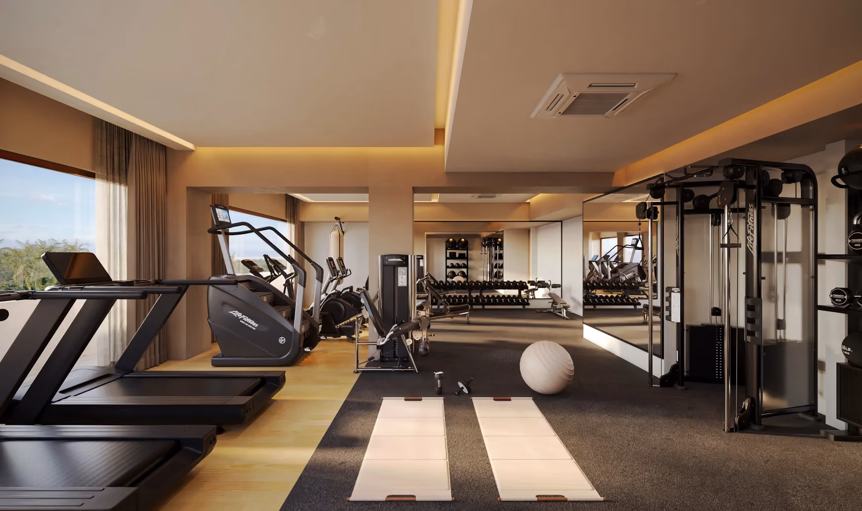 Modern gym interior with two treadmills on the left, elliptical machines behind them, a multi-functional weight machine on the right, two exercise mats and a stability ball on a dark carpeted floor, and a mirrored wall with dumbbell racks in the background.