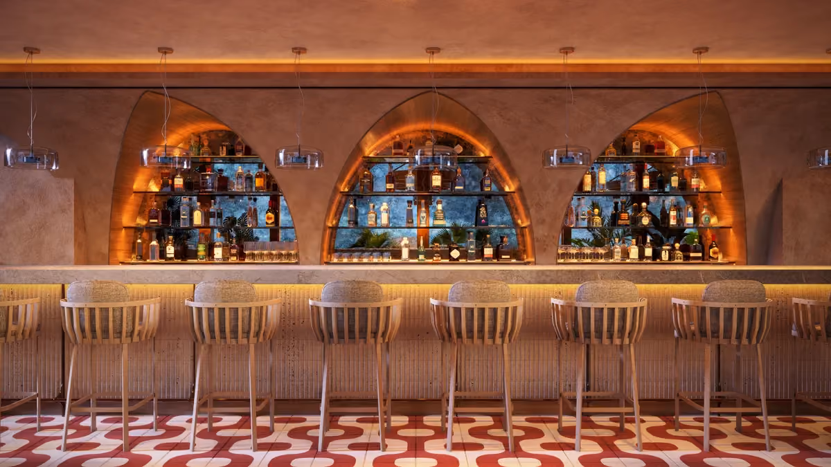 Modern bar interior with seven wooden bar stools facing a long marble countertop, three arch-shaped backlit shelves filled with bottles, decorative plants, and hanging glass pendant lights above the bar, set against a warm, textured wall and retro patterned floor tiles.