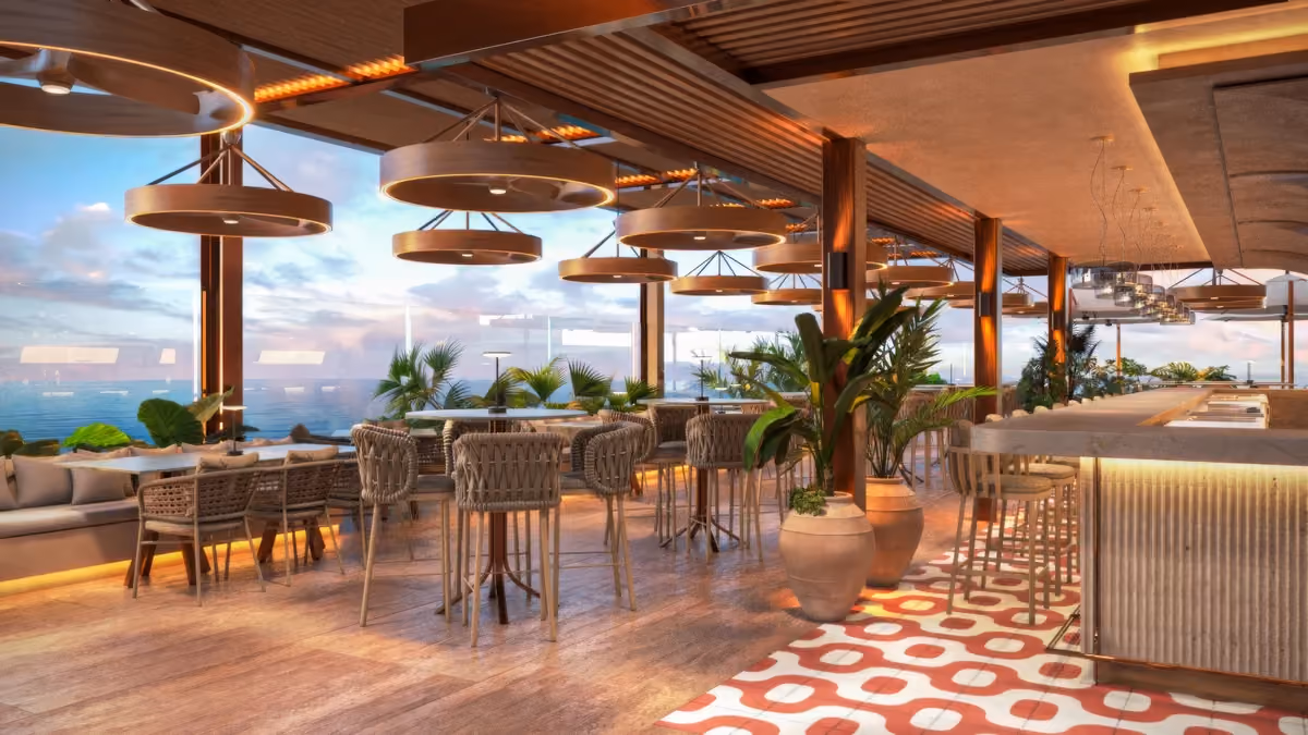 Modern rooftop bar and lounge with wooden furniture, round hanging lights, potted plants, and large windows offering an ocean view at sunset.