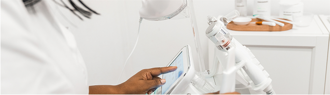 Hand of a person operating a touchscreen on a medical or dental machine in a clinical setting.